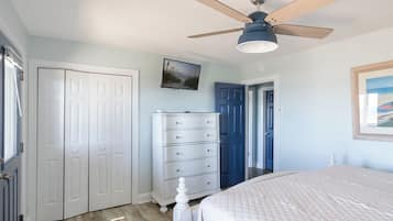 A bedroom with a bed, a dresser, a ceiling fan, and a door leading to another room.