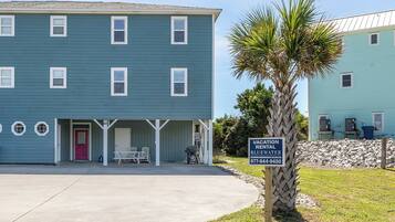 A vacation rental property with a covered outdoor seating area, a red door, and a sign indicating it is a vacation rental in Bluewater.