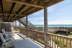 A wooden deck with a view of the ocean, featuring a wooden staircase, seating area, and railings.