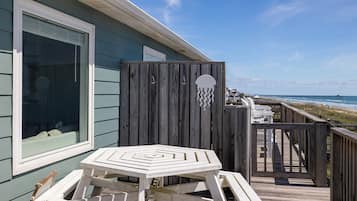 A wooden deck with a white table and chairs, a wooden fence, and a view of the beach and pier.
