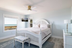 Een slaapkamer met een bed, een bankje, een plafondventilator, een televisie en uitzicht op het strand.