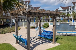 A covered outdoor seating area with benches and a pergola, overlooking a pool and a waterfront view. - Beautiful 2/2 Seascape condo directly on beach! (Galveston)