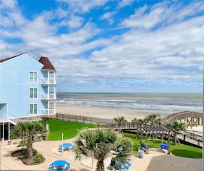 A beachfront hotel with a multi-story building, a beach view, and a wooden boardwalk with seating. - Beautiful 2/2 Seascape condo directly on beach! (Galveston)