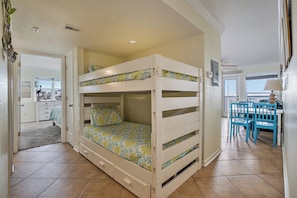 A bunk bed with patterned bedding, a desk with chairs, and a view of the outside. - Beautiful 2/2 Seascape condo directly on beach! (Galveston)