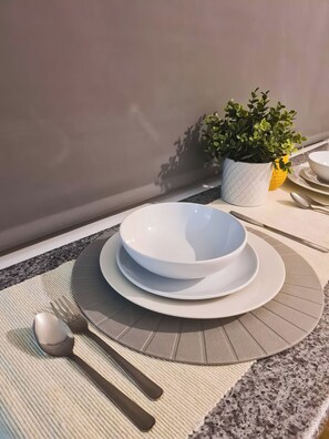 A table set with a white bowl, a plate, a spoon, and a fork, with a small potted plant on the table. - Modern 1-bedroom flat in City Centre, Leicester. (Leicester)