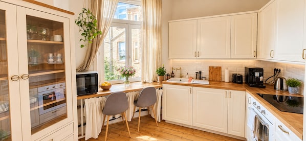 Cocina con armarios blancos, encimera de madera, estufa, microondas y ventana con cortinas.