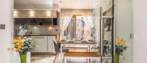 A modern kitchen with a glass partition, a dining area with a table set for four, and a view of the outside.