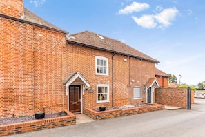 A two-story brick house with a front door, a small porch, and a garage. - Historic 3-Bed Town House Sleeps 6 · Carport Parking · Fishbourne (Fishbourne)