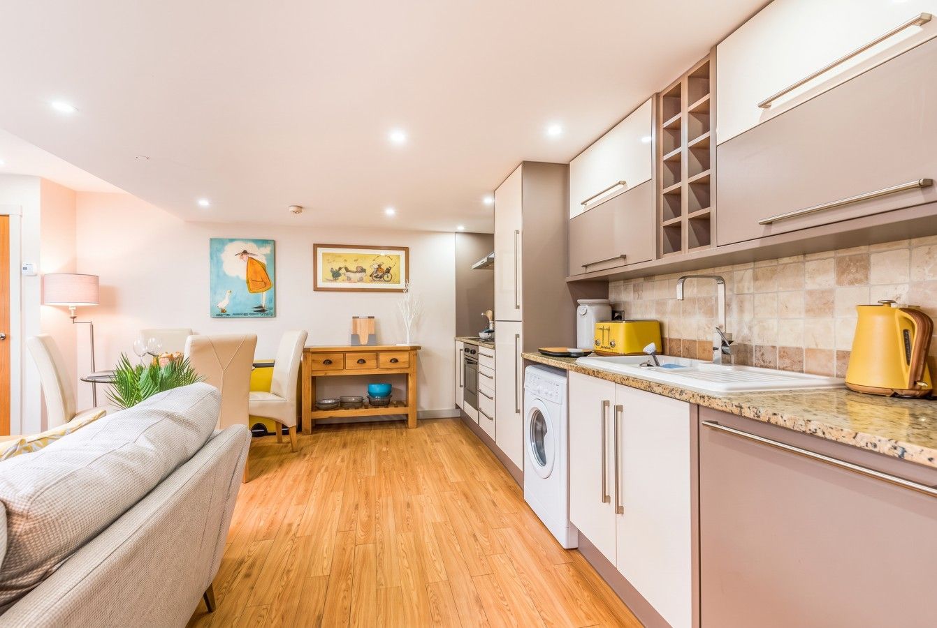 A modern kitchen with a washing machine, a dining area with a sofa, and a small table with a lamp.