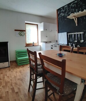 A compact kitchen with a dining table, chairs, a stove, and a window with curtains. - Cozy rugged apartment for hiking adventures on the Dolomites - Casa Val de Rore (Trentino-Alto Adige)