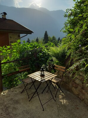 An outdoor seating area with a table and chairs, surrounded by greenery and a mountain backdrop. - Cozy rugged apartment for hiking adventures on the Dolomites - Casa Val de Rore (Trentino-Alto Adige)