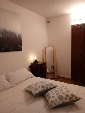 A bedroom with a bed, pillows, a nightstand with a lamp, a mirror, and a door. - Cozy rugged apartment for hiking adventures on the Dolomites - Casa Val de Rore (Trentino-Alto Adige)