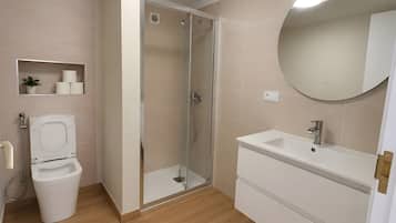 A modern bathroom with a toilet, a glass-enclosed shower, a sink, and a mirror.