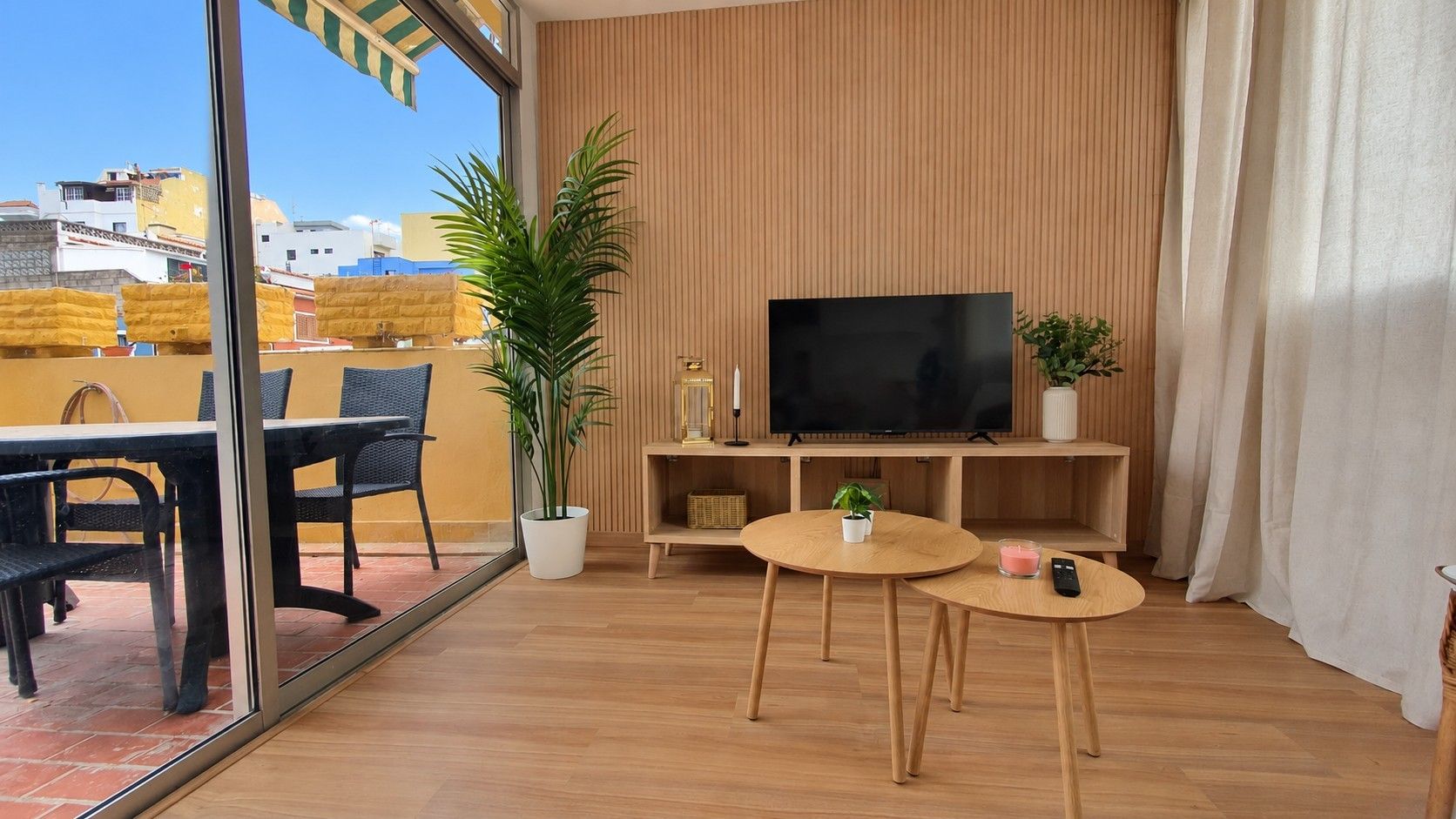 A modern living room with a flat-screen TV, wooden furniture, and a potted plant.