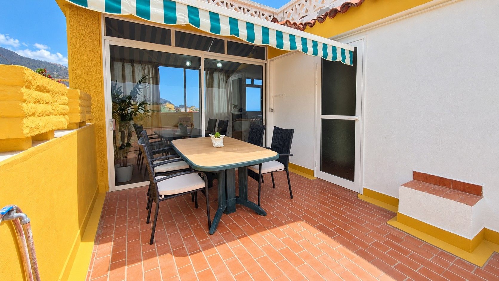 Un patio con una mesa, sillas, una planta en maceta y vistas de los alrededores.