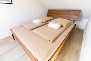 Ein Bett mit Holzrahmen, zwei Kissen und zwei gerollte Handtücher.