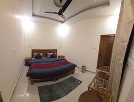A bedroom with a bed, a ceiling fan, a small wooden nightstand, a wicker chair, and a door.
