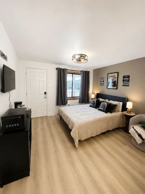A bedroom with a bed, a desk, a television, and a window with curtains.