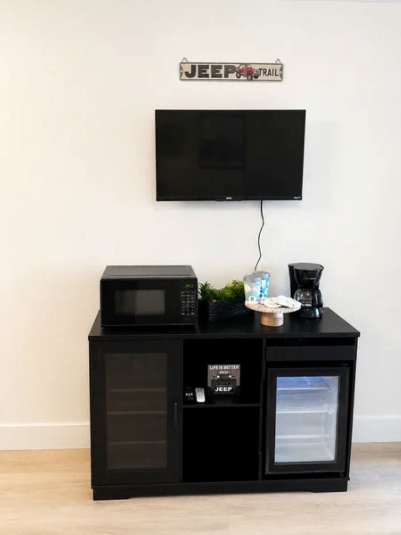 A black entertainment unit with a television mounted above it, a microwave, a coffee maker, and a small refrigerator.