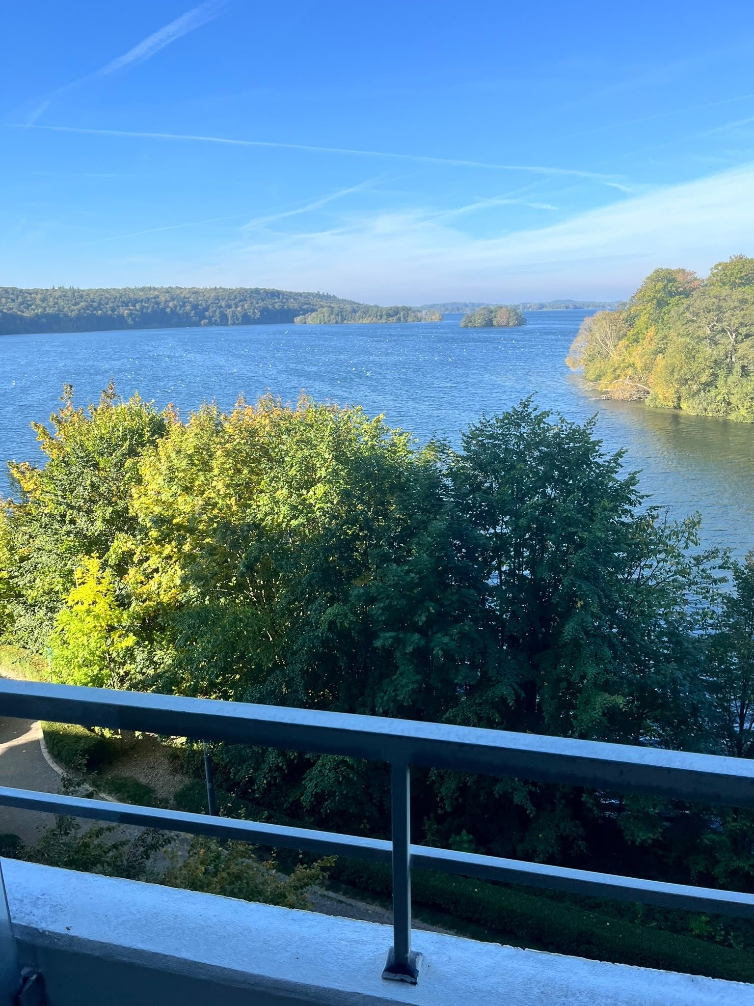 Vista da un balcone su una distesa d'acqua, con alberi sullo sfondo e una costa in lontananza.