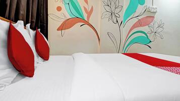 A hotel room with a bed, red and white pillows, and a wall with abstract floral wall art.