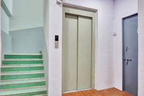 A hallway with a green staircase, a closed door, and a light switch on the wall. - Hotel O Aru Sai (Pune)