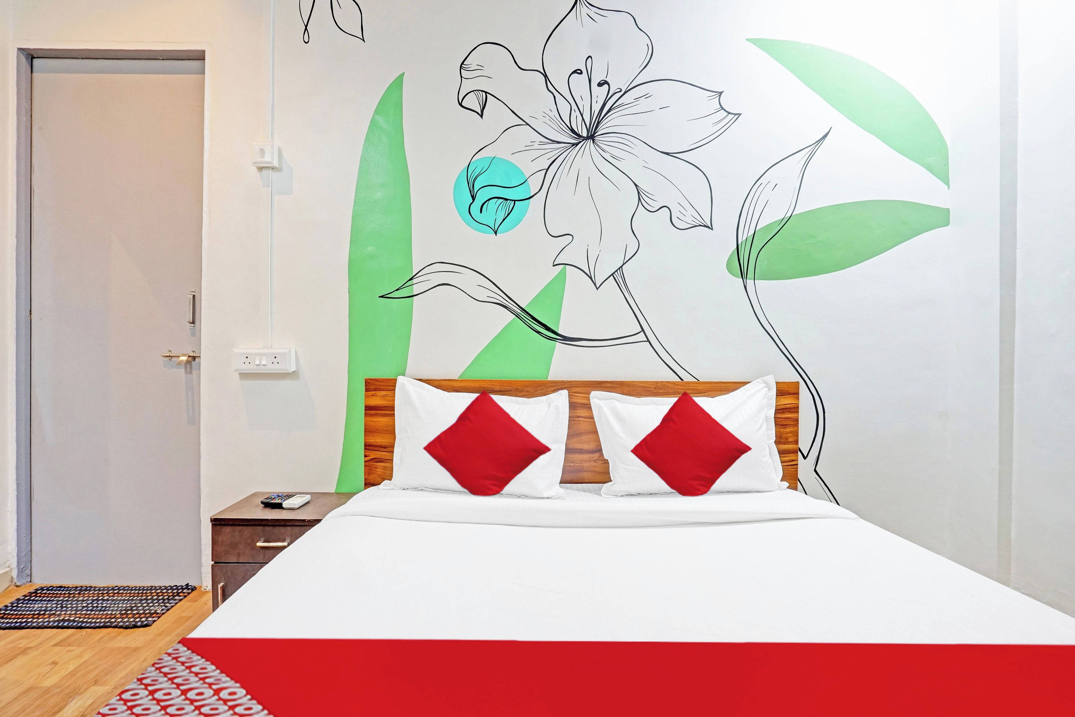 Una camera da letto con un letto, un comodino, una parete con un murale floreale e una porta.