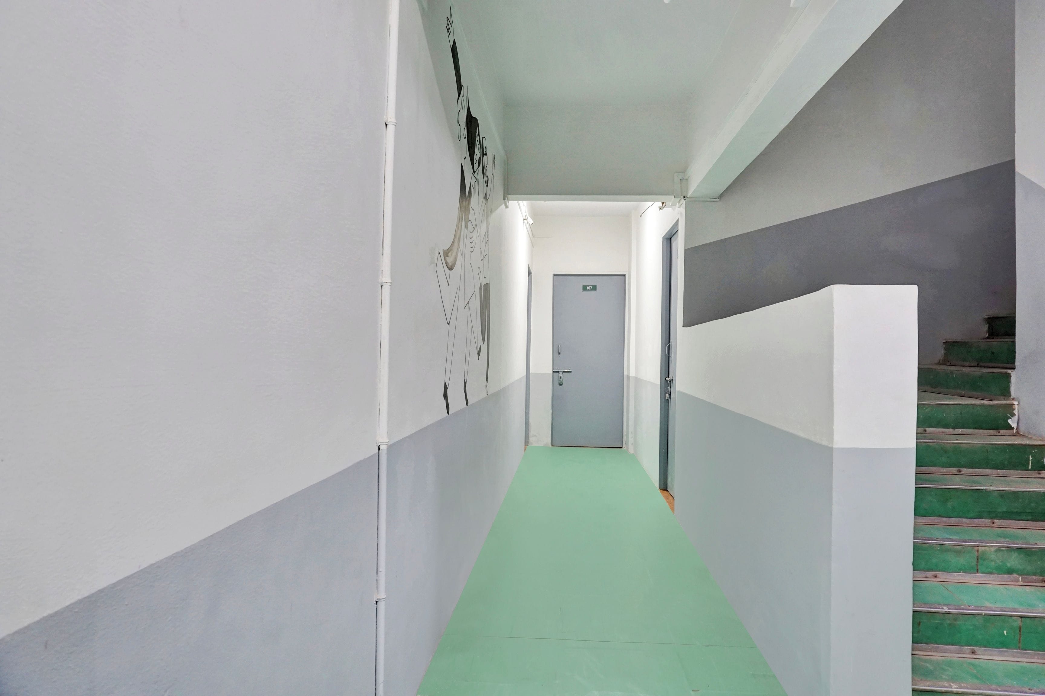 Un pasillo estrecho con alfombra verde, paredes blancas y una puerta gris al final.