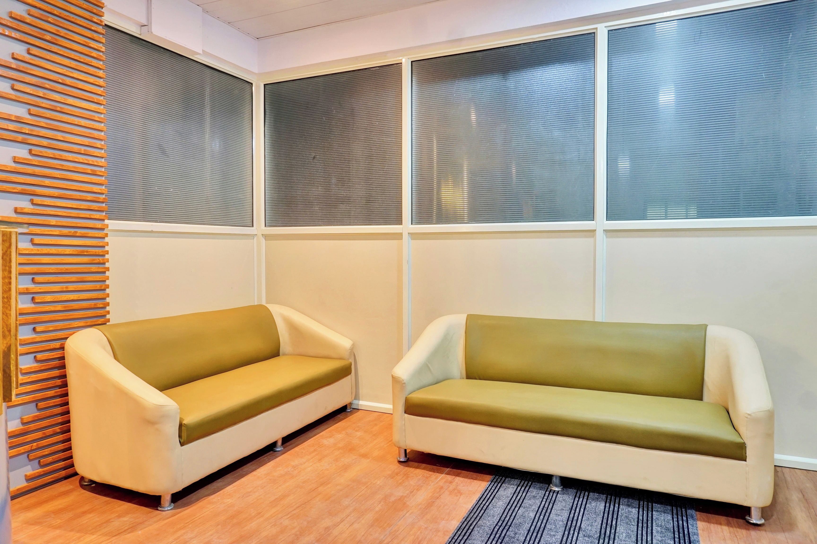A room with two sofas, a wooden slat wall, and large windows with blinds.