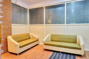 A room with two sofas, a wooden slat wall, and large windows with blinds. - Hotel O Aru Sai (Pune)