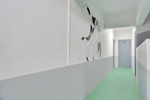 A corridor with a green carpet, white walls, and a door labeled '101'. - Hotel O Aru Sai (Pune)