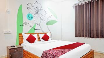Habitación de hotel con cama, mesita de noche, cómoda de madera, pared con un mural floral y ventana con cortinas.
