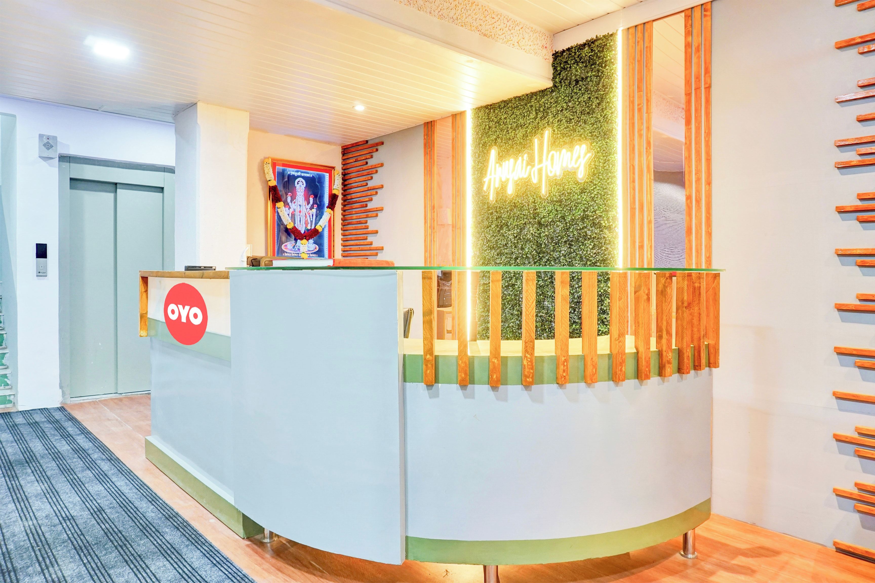 Een receptiebalie met een groene muur, een neonbord, een ingelijst beeld en een houten lattenstructuur aan de rechterkant.