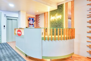 A reception desk with a green wall and a neon sign, a framed picture, and a wooden slat design on the right. - Hotel O Aru Sai (Pune)