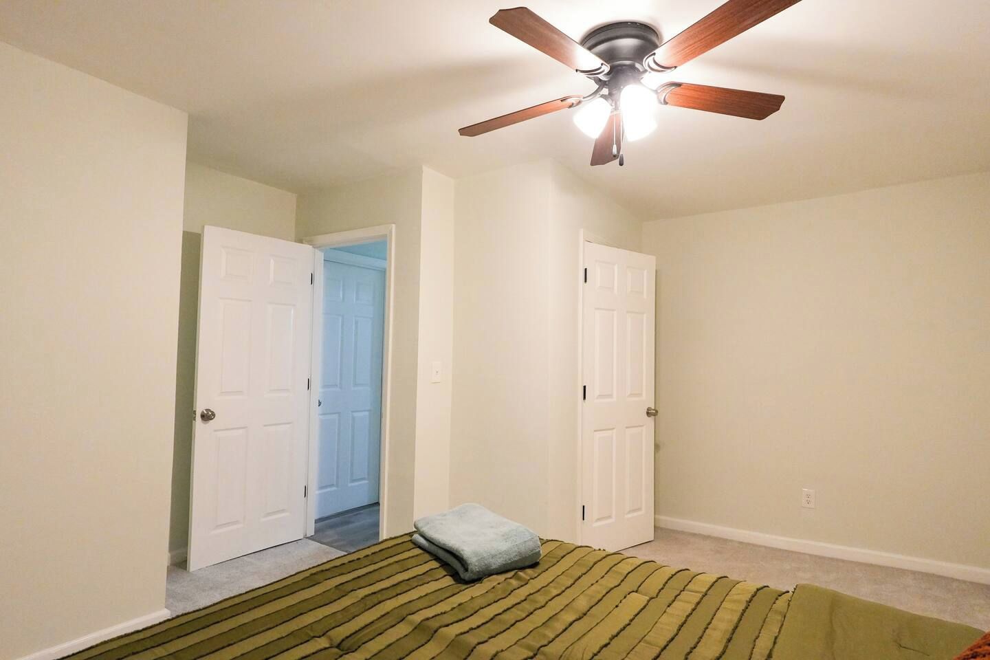 A bedroom with a bed, a ceiling fan, and two doors leading to other rooms.