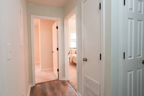 Un couloir avec un sol recouvert de moquette, qui mène à une chambre à coucher équipée d’un lit et d’une fenêtre.