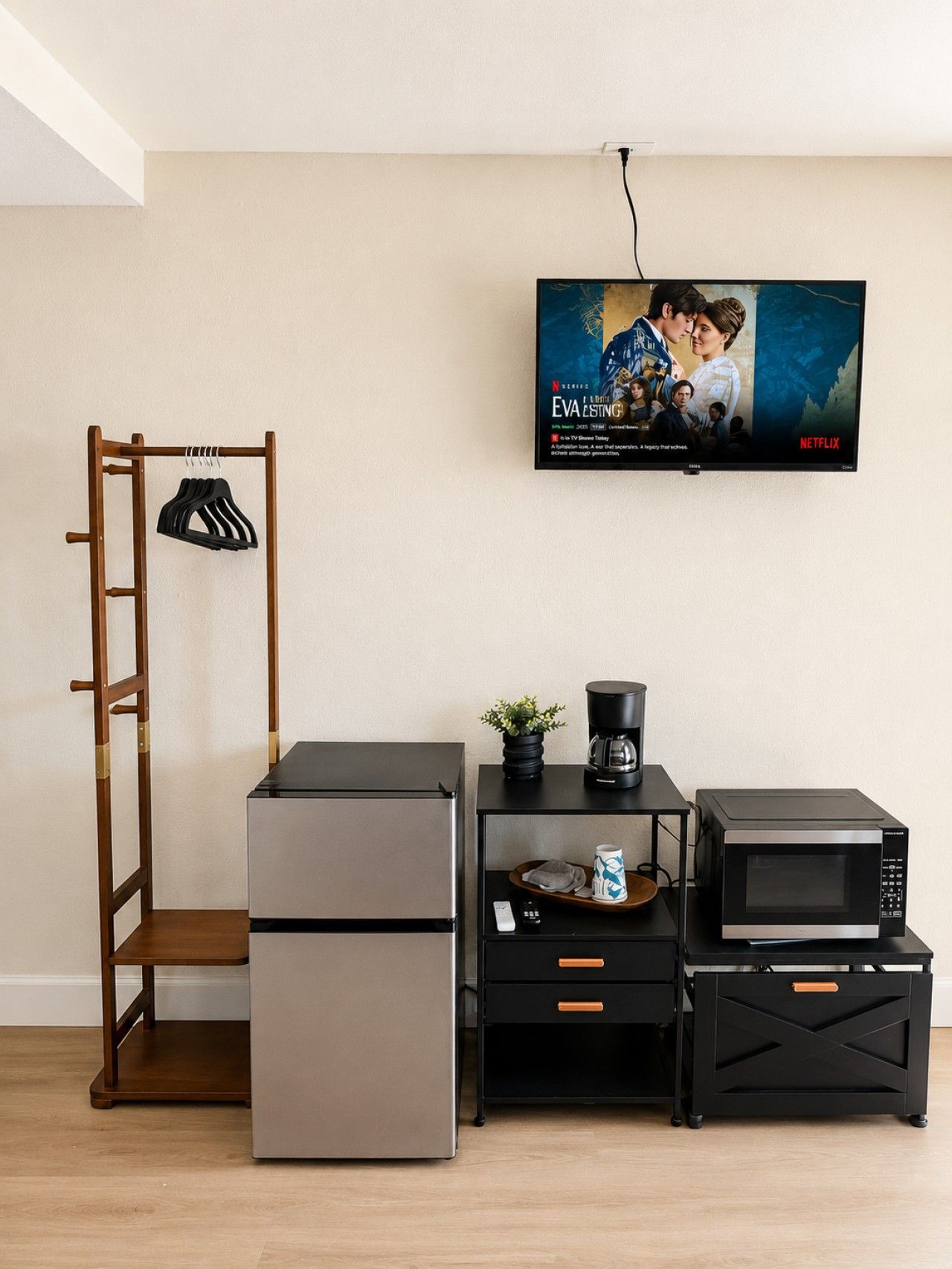A kitchenette with a refrigerator, microwave, coffee maker, and a TV displaying a movie poster.