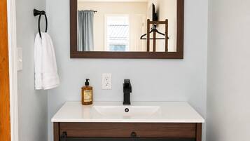 Un baño con un lavamanos blanco, un mueble de madera con diseño de cruz, un perchero y un espejo con marco negro.