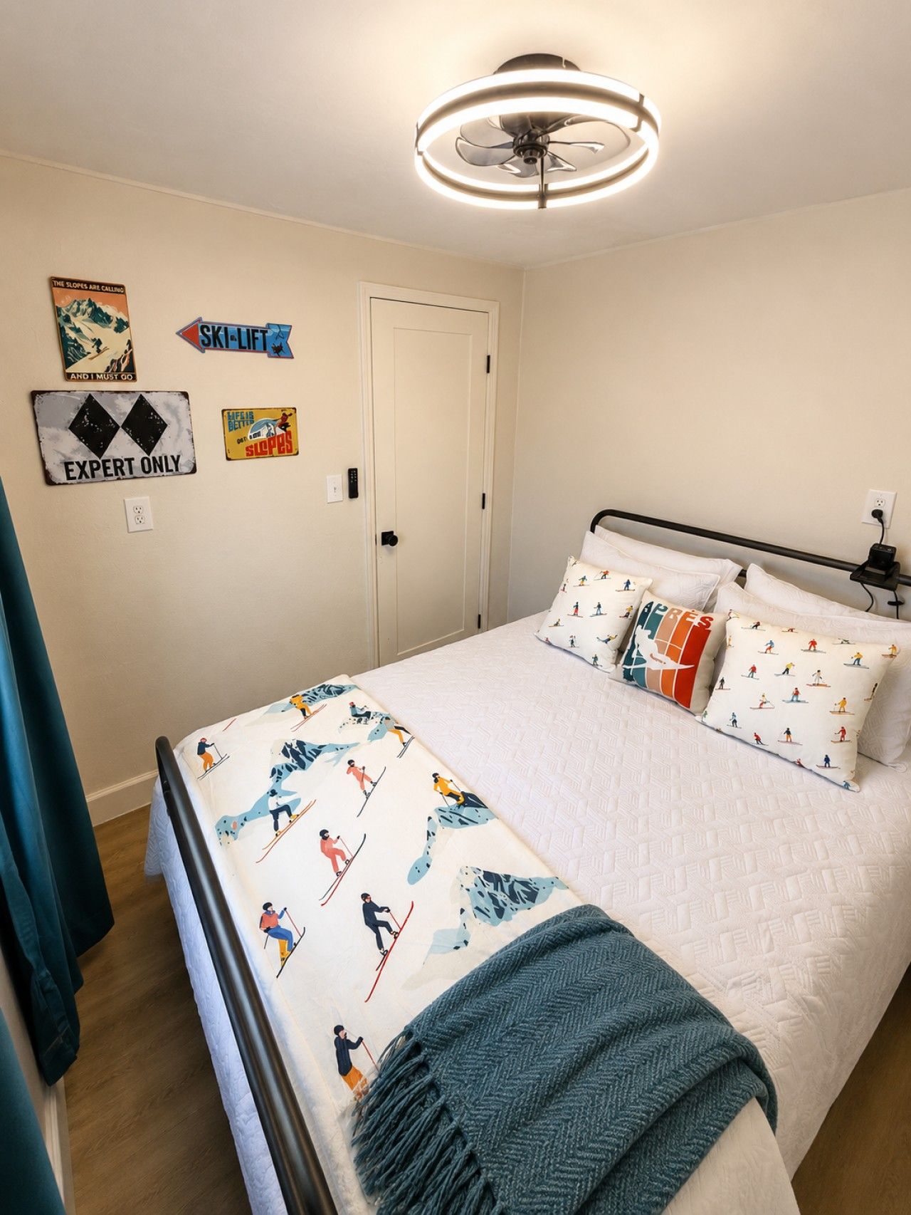 Un dormitorio con cama, almohadas con diseño de esquí, ventilador de techo y decoraciones en la pared, incluyendo un cartel de telesilla.