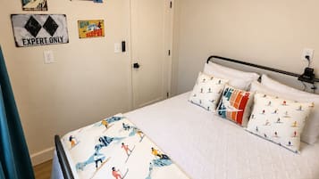 Un dormitorio con cama, almohadas con diseño de esquí, ventilador de techo y decoraciones en la pared, incluyendo un cartel de telesilla.