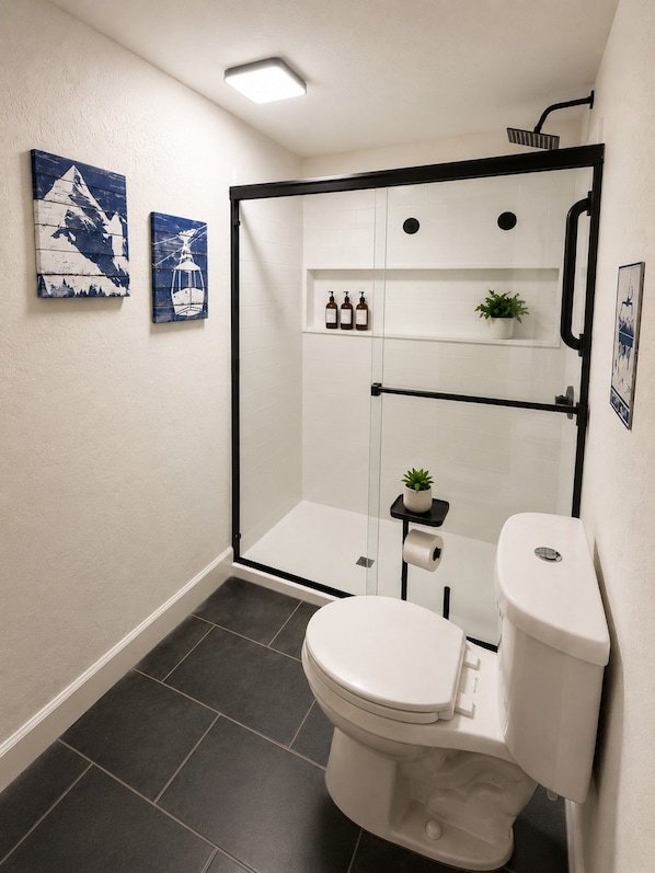 A modern bathroom with a glass-enclosed shower, a toilet, and a shelf with toiletries.