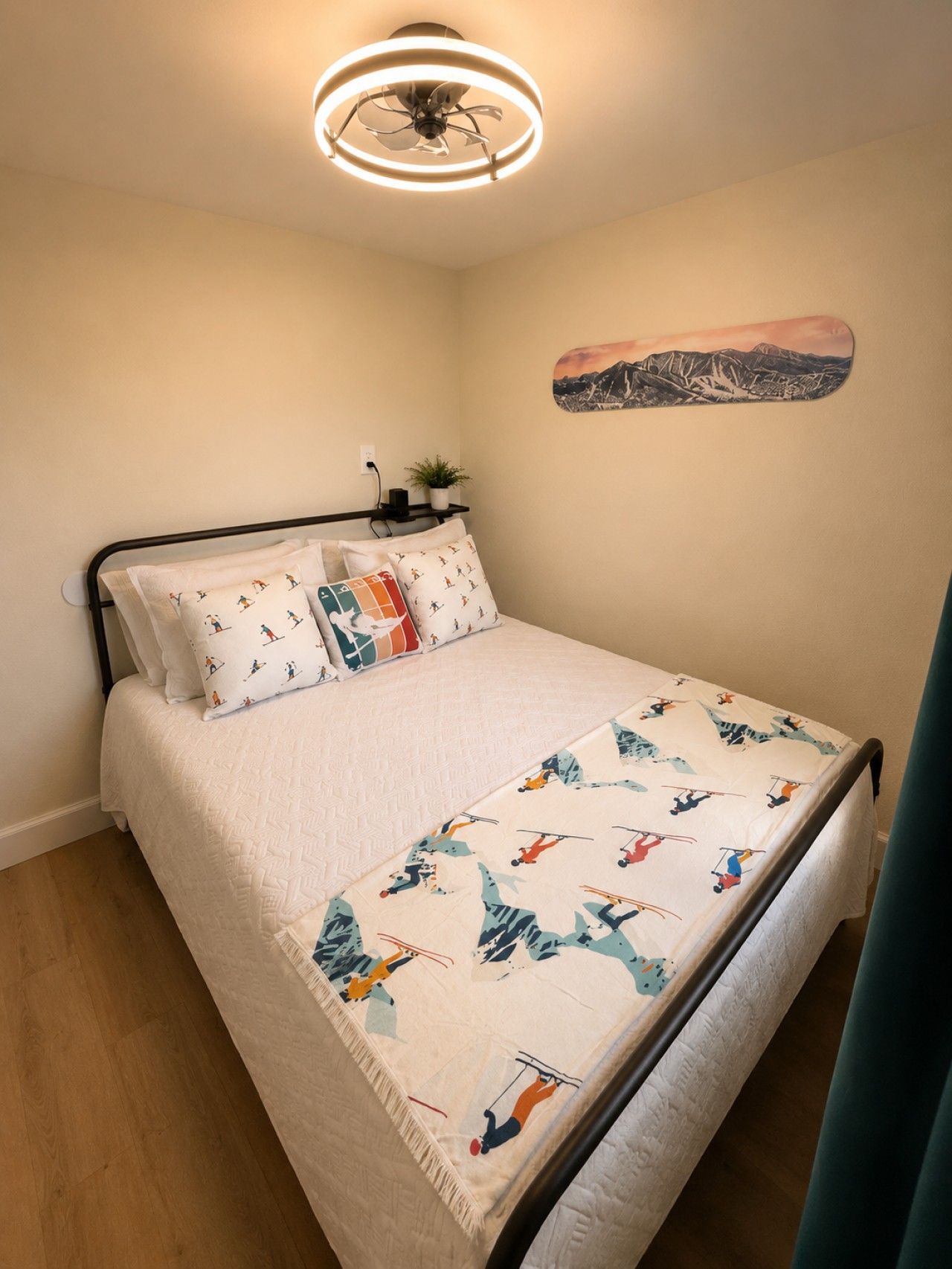 A bedroom with a bed, pillows, a ceiling fan, a wall-mounted plant, and a mountain landscape artwork.