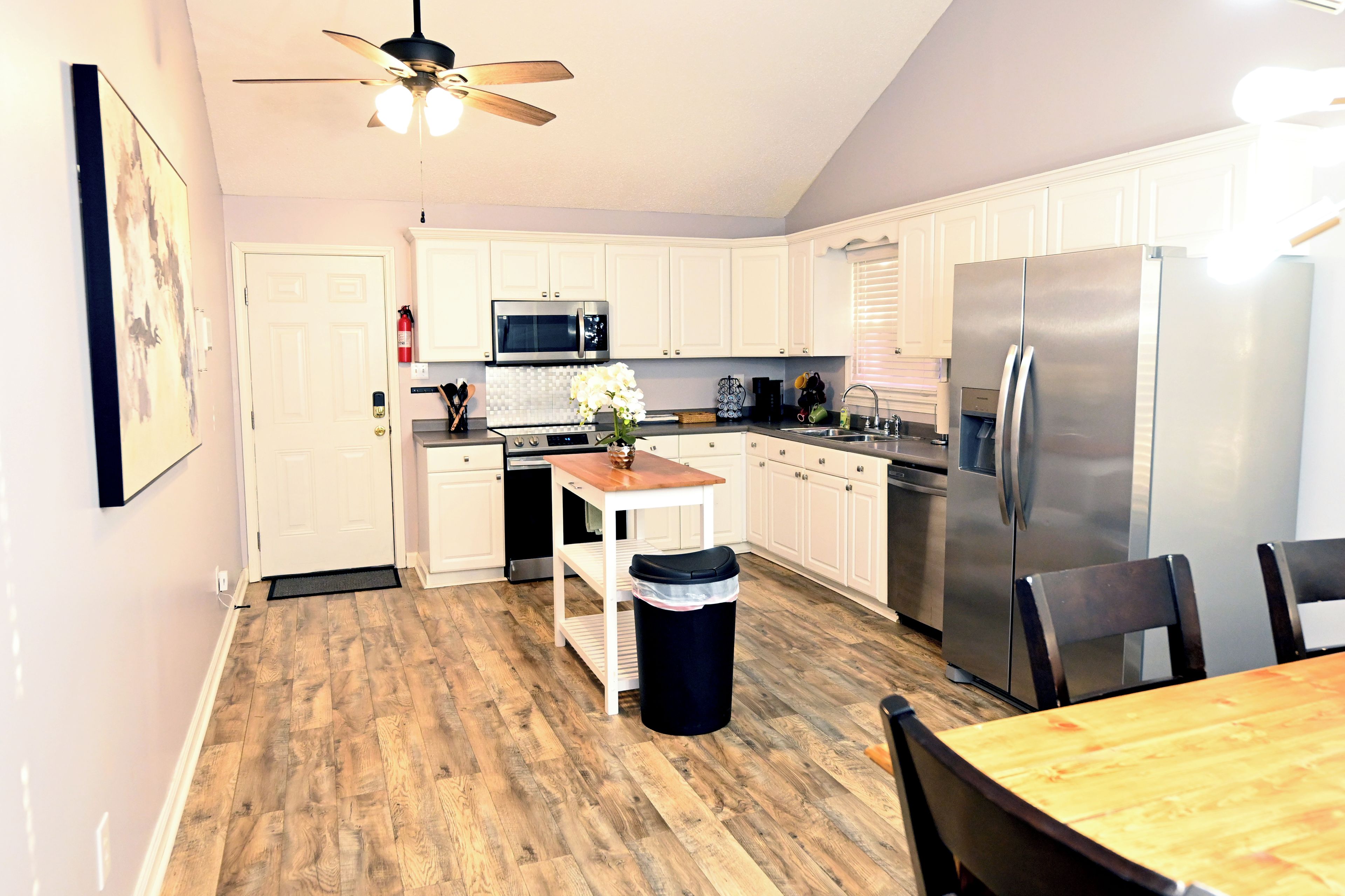 A kitchen with white cabinets, a stainless steel refrigerator, a microwave, and a ceiling fan.