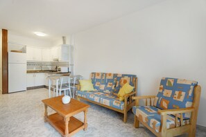 Een gezellig, compact ingerichte ruimte met een kitchenette, een bank, een fauteuil en een tafeltje.