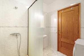 Een badkamer met een douche, een wastafel en een houten deur.