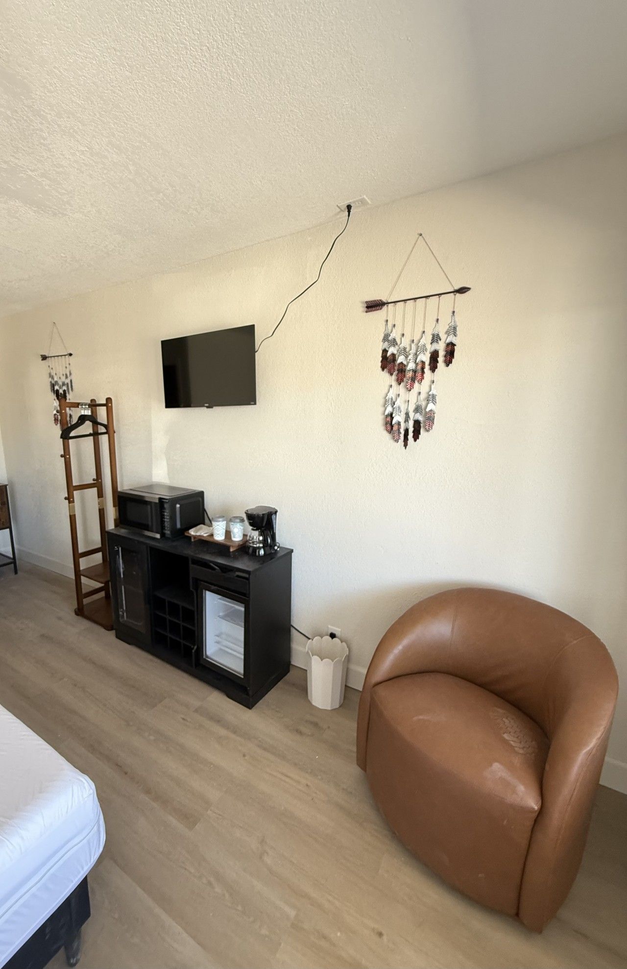 Una stanza con una TV a schermo piatto montata a parete, un mobile nero contenente una macchina per il caffè, una poltrona in pelle marrone e un addobbo appeso con piume.
