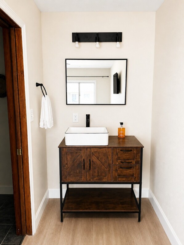 A bathroom with a wooden vanity, a white sink, a mirror, and a towel rack.