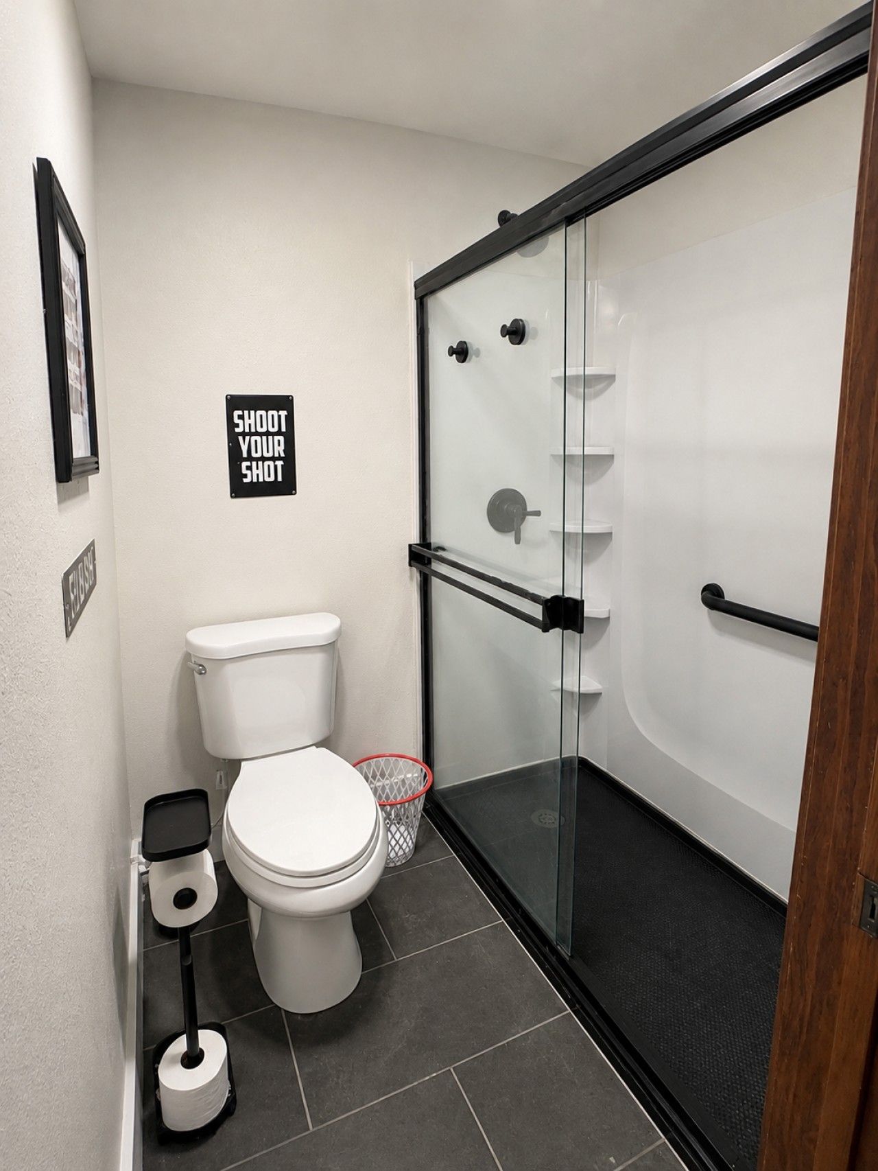 A modern bathroom with a toilet, a glass shower enclosure, and a 'SHOOT YOUR SHOT' sign on the wall.