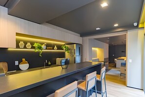 Eine moderne Küche mit dunkler Arbeitsplatte, weißen Stühlen und einem eingebauten Backofen.
