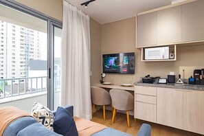 A modern living room with a sofa, a television, and a dining area with chairs and a kitchen counter. - Prime Bela Vista - Av. Paulista - Sírio (São Paulo)